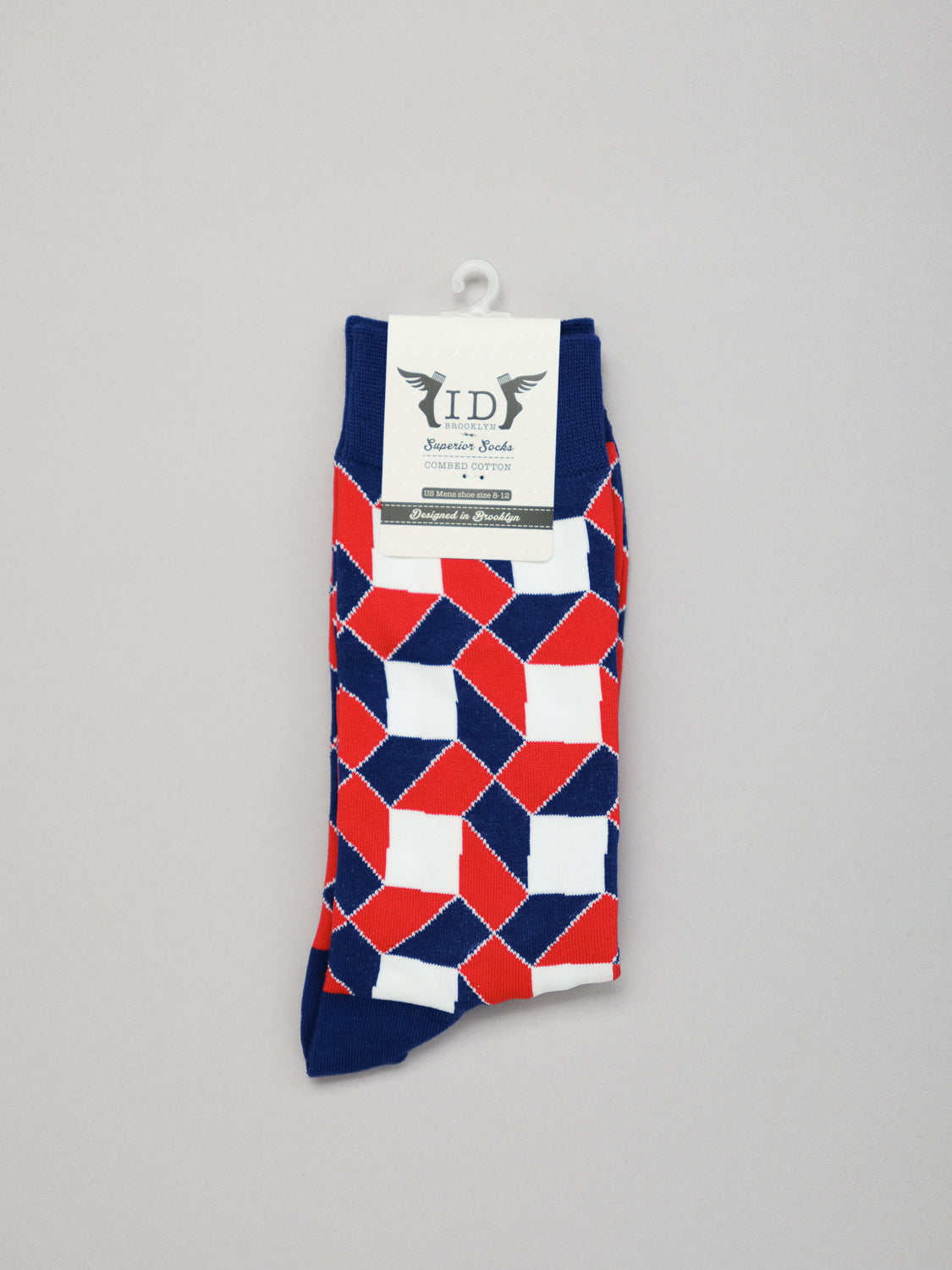 The Octto Graphic Socks by ID Menswear feature a vibrant red, white, and blue geometric pattern. Made from soft combed cotton, they fit mens shoe sizes 8-12. Neatly folded with a branded white label and display hook, theyre set against an elegant light gray background.