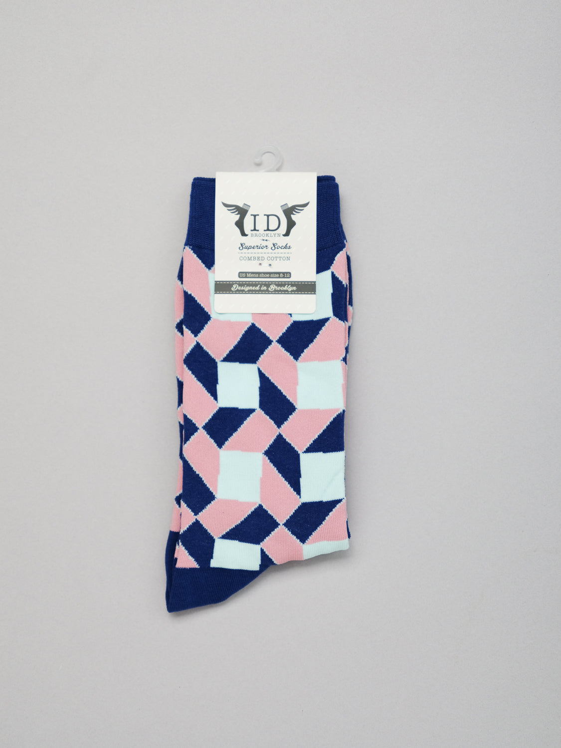 A pair of Octto Graphic Socks with a vibrant geometric pattern in pink, blue, and white, made from combed cotton. Neatly folded with an ID Menswear logo label, they fit mens shoe sizes 8-12 and rest on a plain background.