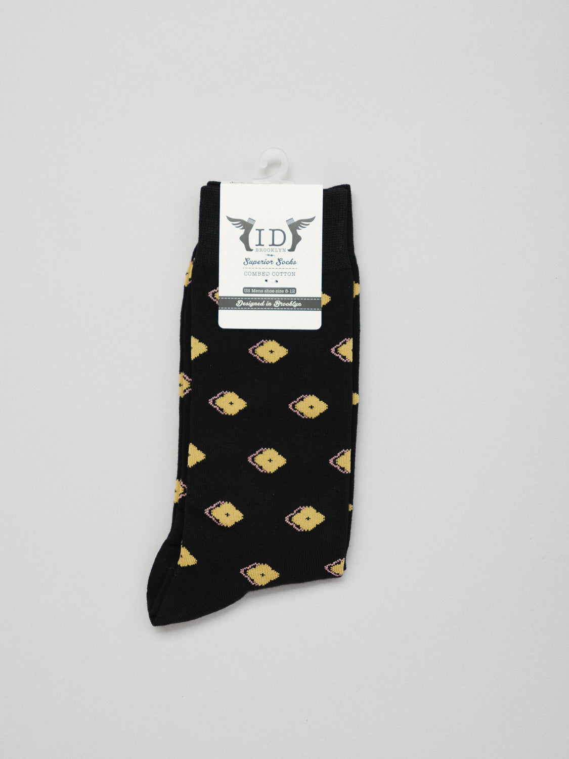A pair of comfortable black socks with a yellow geometric pattern, reminiscent of Japanese designs, from ID Menswear. Crafted from combed cotton, they feature Keda Graphic Socks branding at the top. Neatly folded, they come with a small white hanger attached.