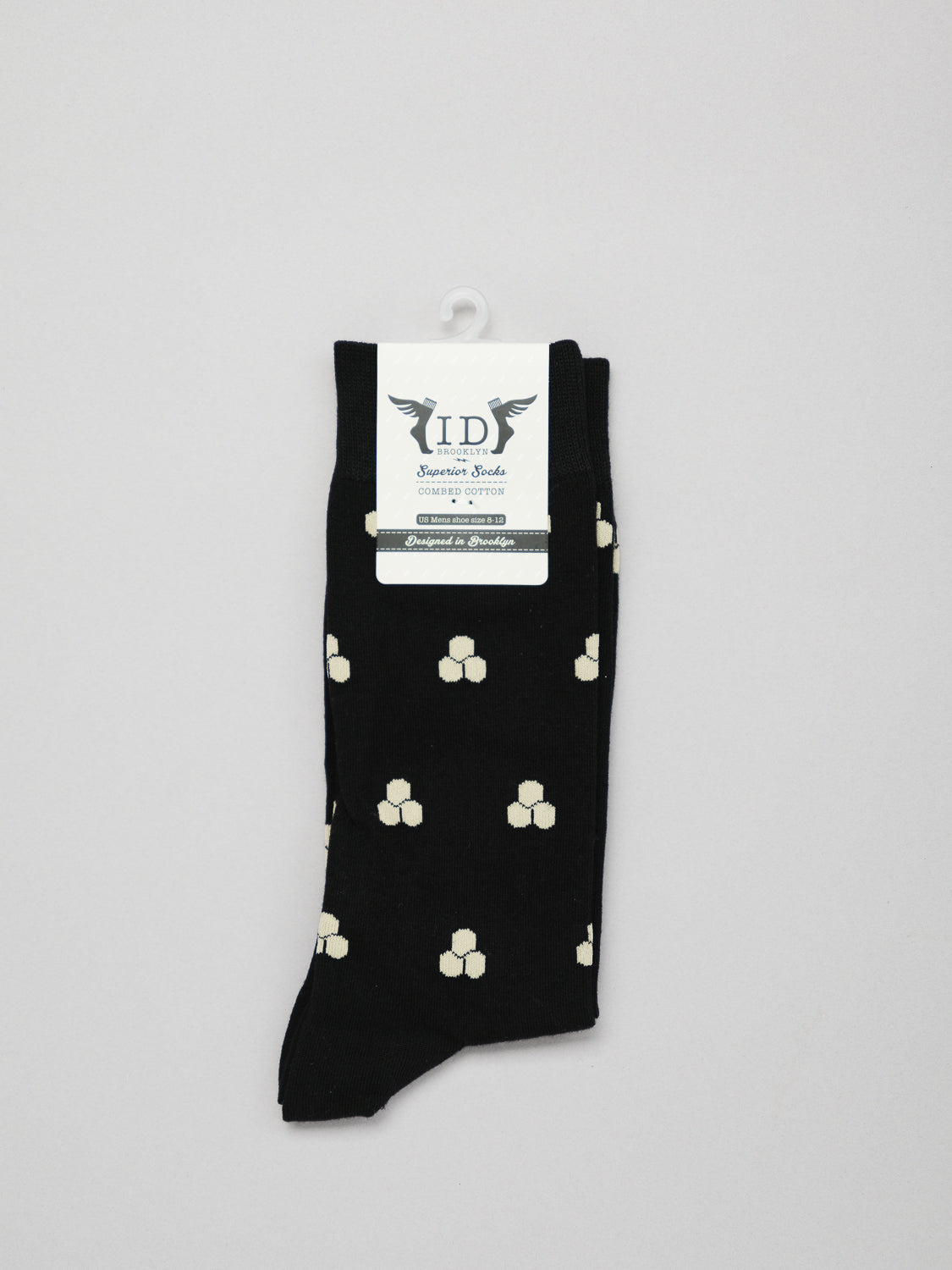 Mae Graphic Socks by ID Menswear are black with a white geometric pattern, featuring small square clusters. Made from premium combed cotton for comfort, theyre packaged with a white tag displaying the logo and description, hanging on a plain white background.