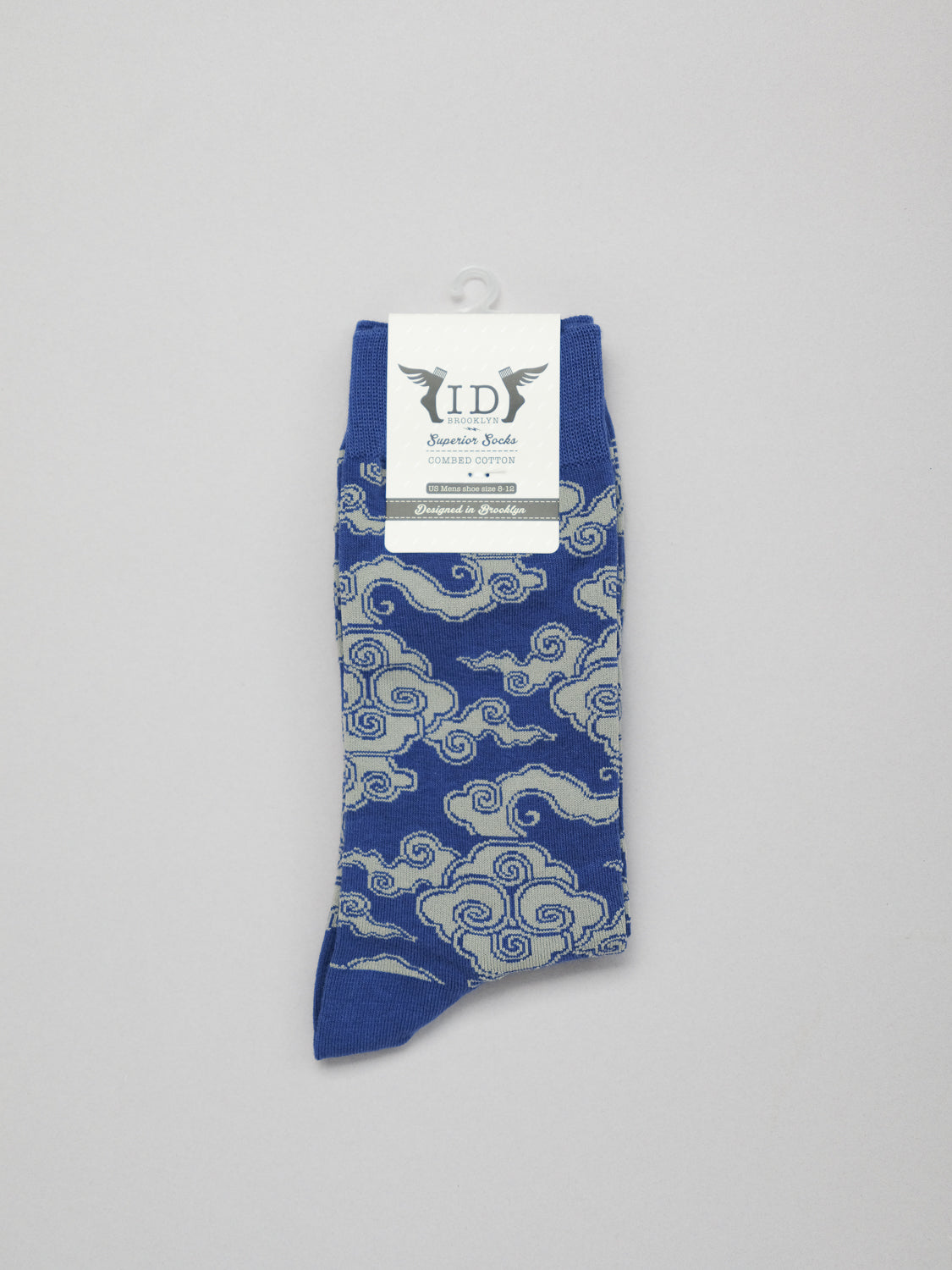 Cloud Graphic Socks from ID Menswear feature an elegant swirling white cloud pattern on blue combed cotton. These breathable socks offer a comfortable stretch fit and are presented against a light gray background.