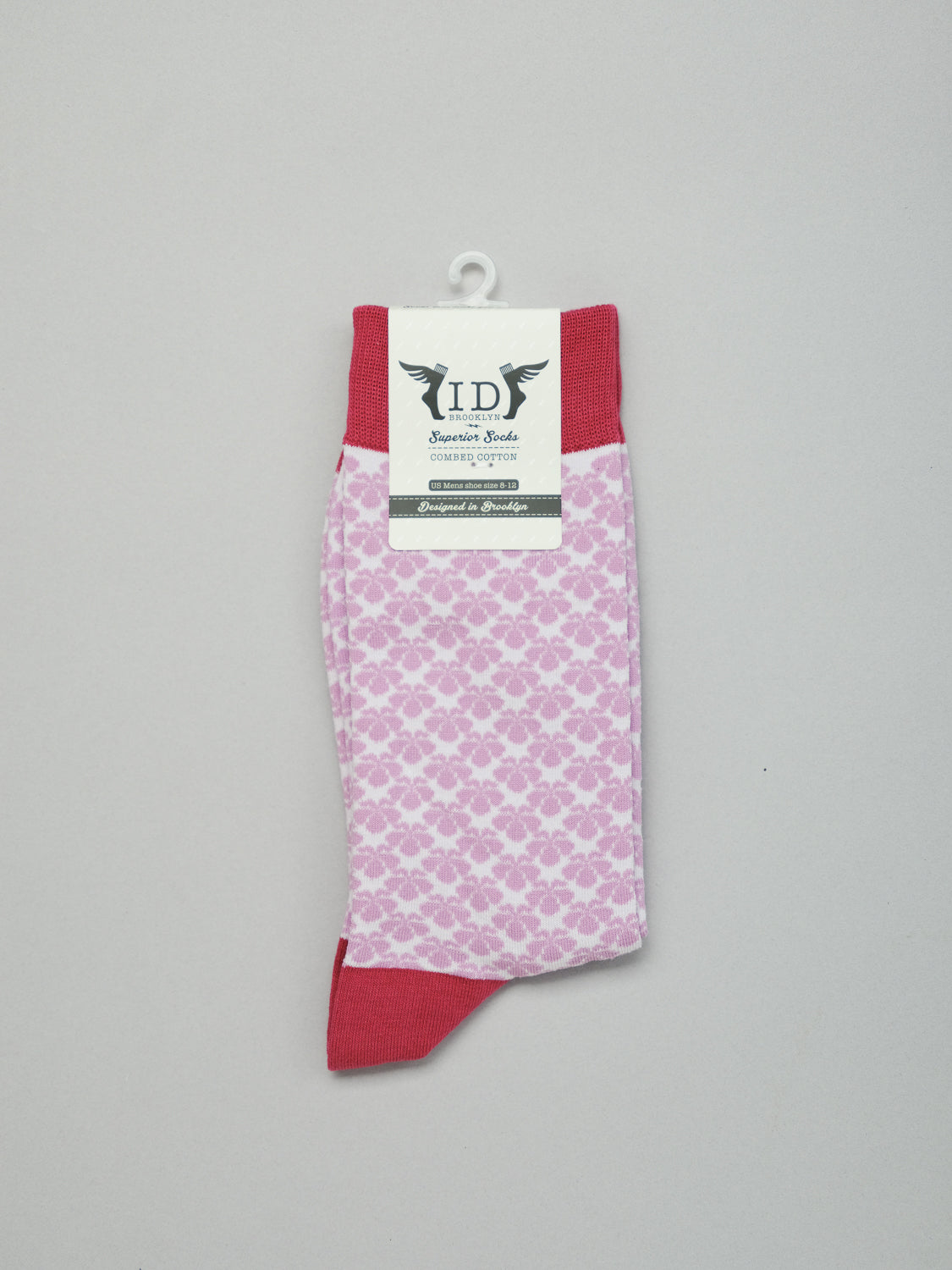 The Toyo Graphic Socks by ID Menswear are pink combed cotton with an abstract design inspired by Japanese art. Featuring red toes and cuffs, they have a wing-logo label. Displayed against a plain light gray background.