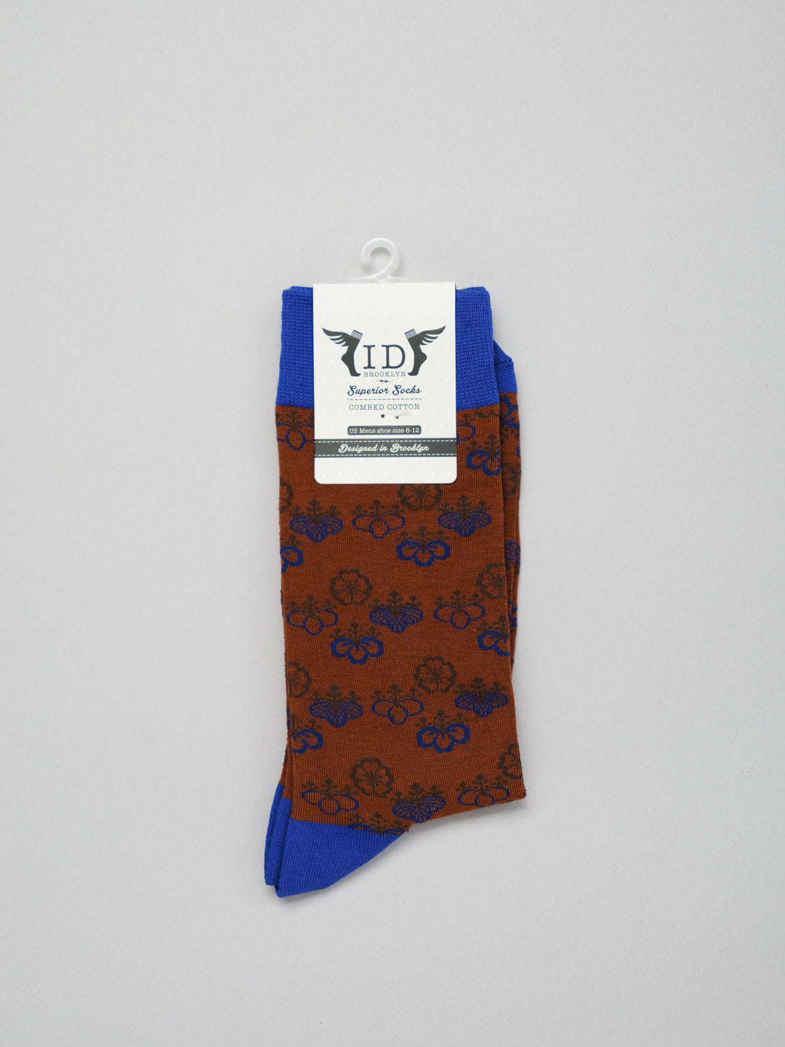 The Giri Graphic Socks by ID Menswear are brown with a blue heel and toe, showcasing a stylish Japanese floral and bicycle design, neatly folded with a display hook attached to the label.