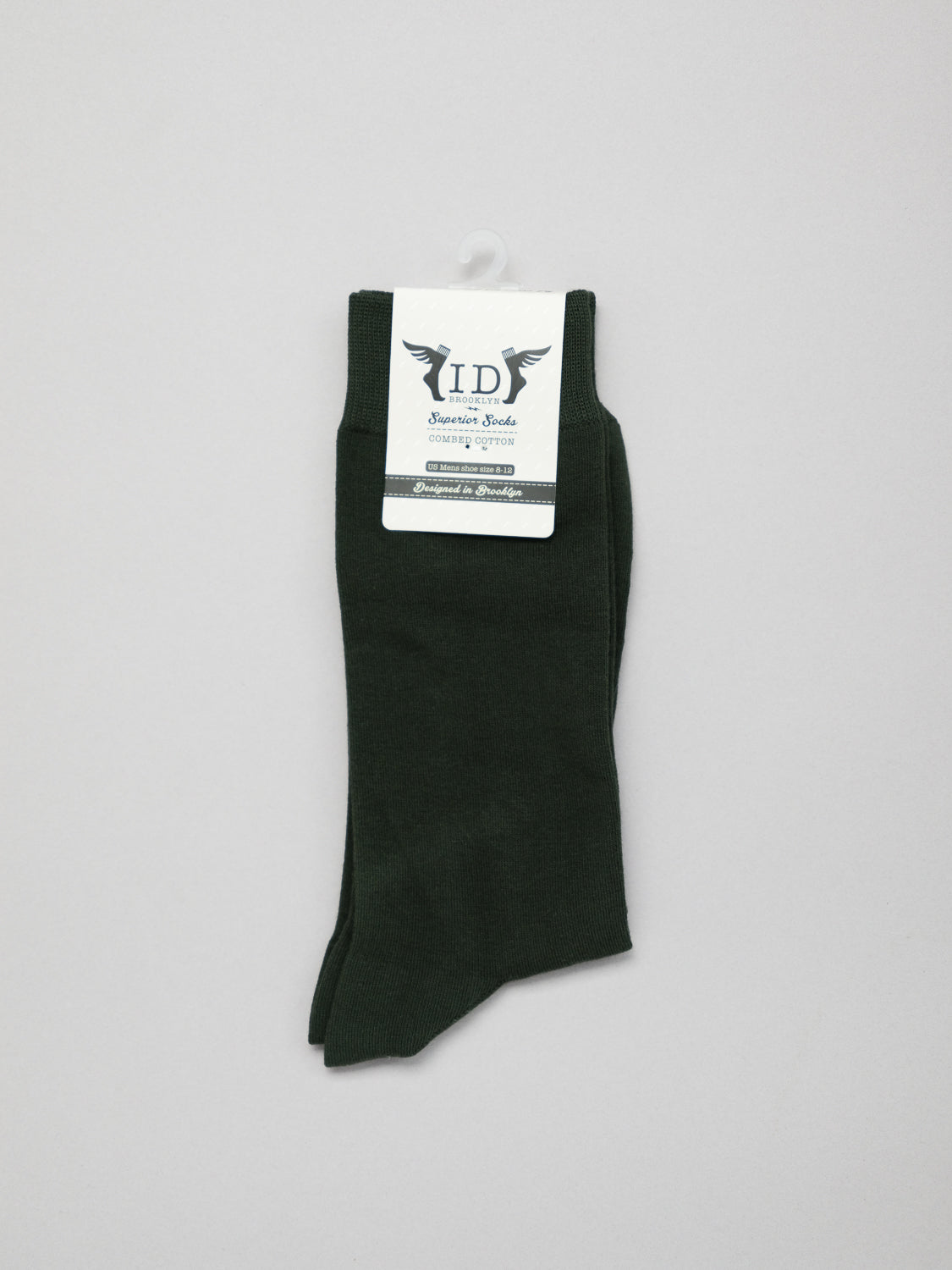 Dark green cotton ID Cotton Socks by ID Menswear, with a label showcasing a small winged logo and details about their breathable nature for all-day wear, hang on a white hook against a light gray background.