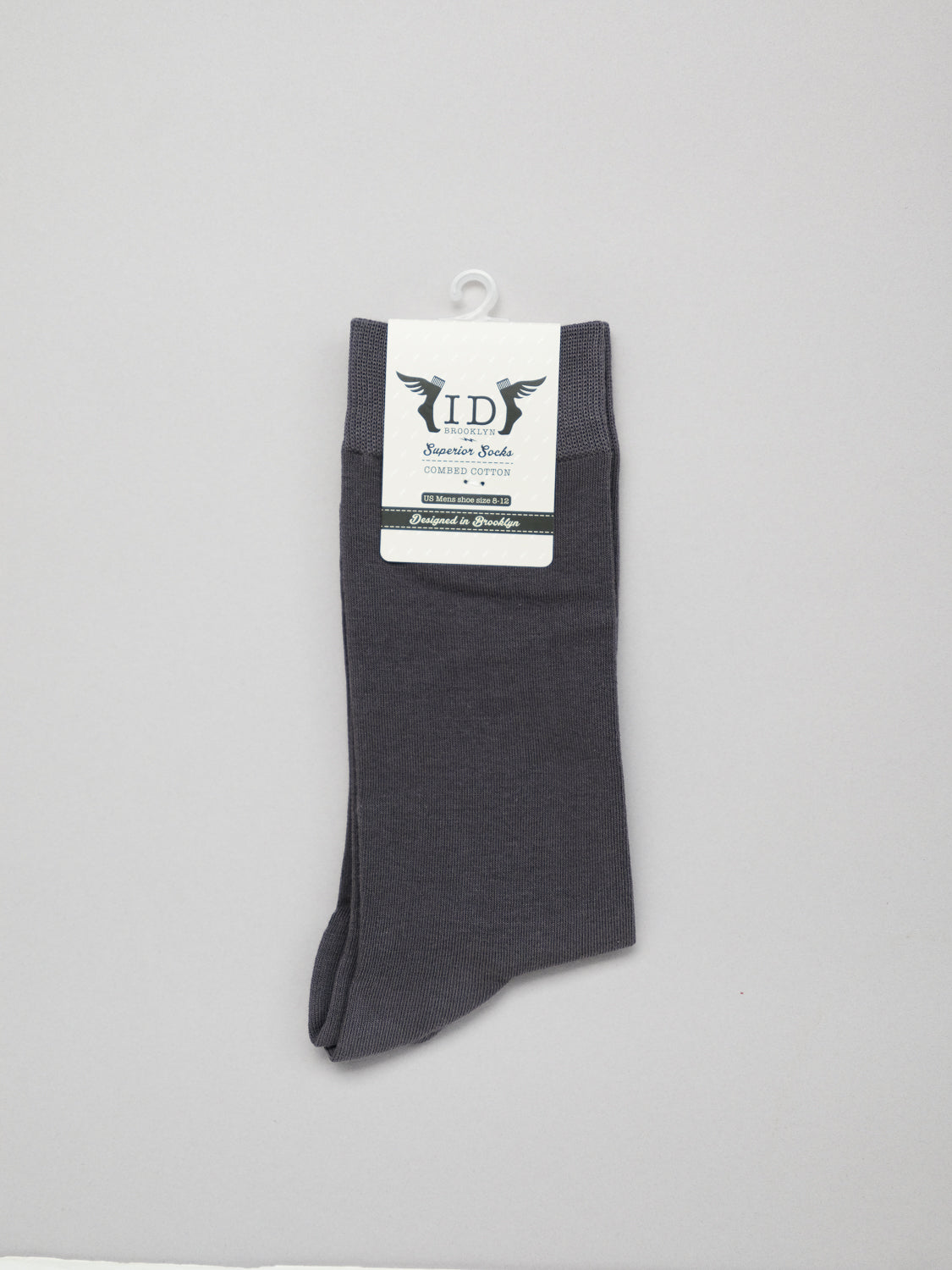 A pair of ID Cotton Socks by ID Menswear, ideal for all-day wear in dark gray, hangs on a plastic hook. The breathable socks are folded with a white and green label featuring text and designs against a light gray backdrop.