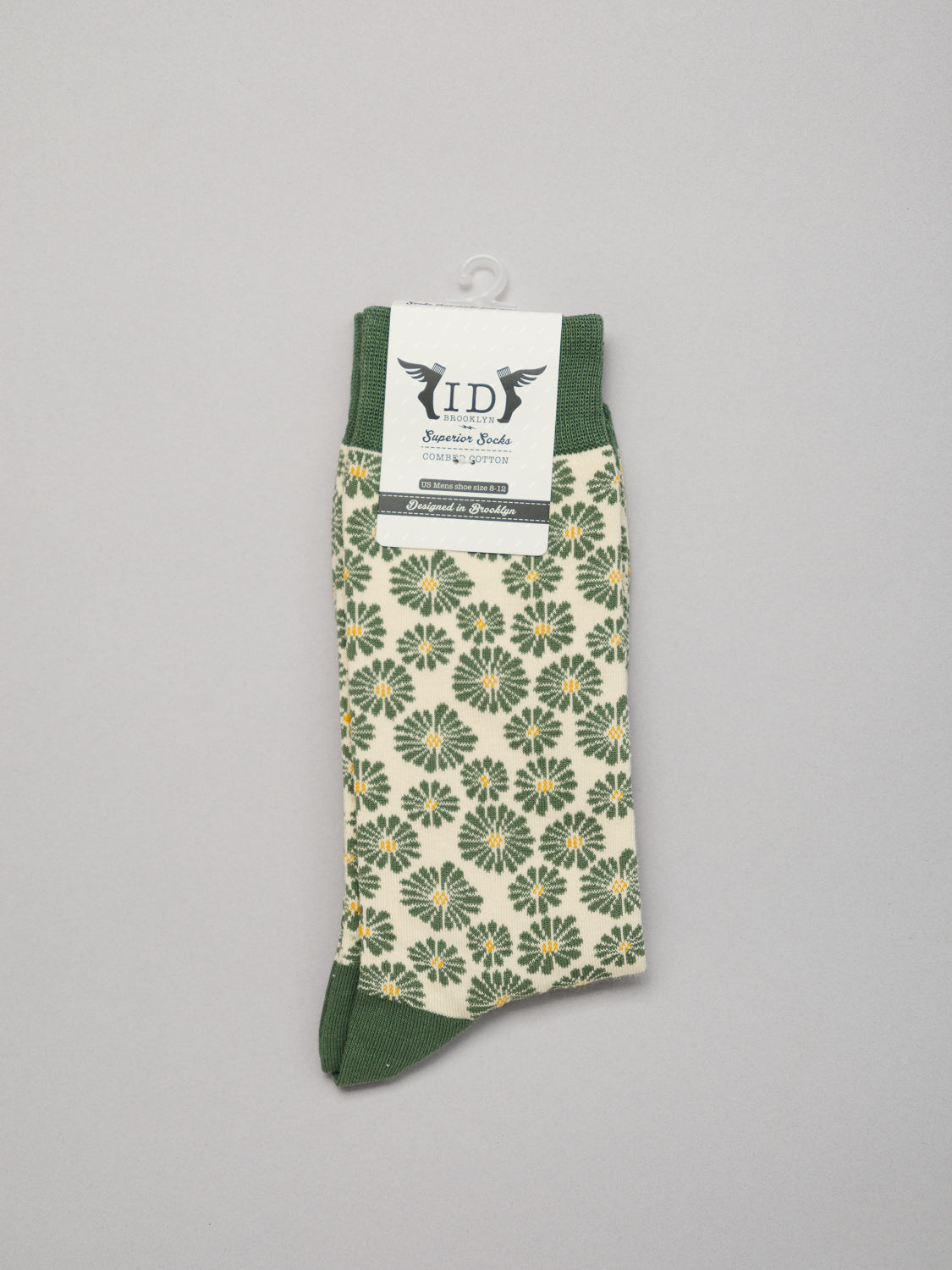 Introducing the Beckia Graphic Socks by ID Menswear: a pair featuring green and yellow floral patterns on white, crafted from premium combed cotton with breathable green cuffs, heels, and toes. A sleek white label displays brand details on a plain surface.