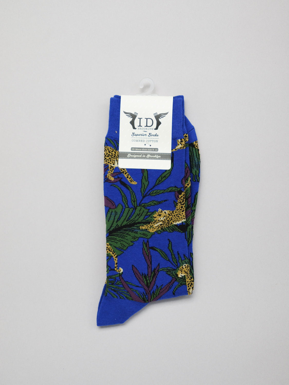 The single blue Jungle Graphic Sock features a jungle pattern of cheetahs in lush green foliage, made from soft combed cotton. Packaged flat with a white label on top, it is branded ID Menswear and Seasons Socks.