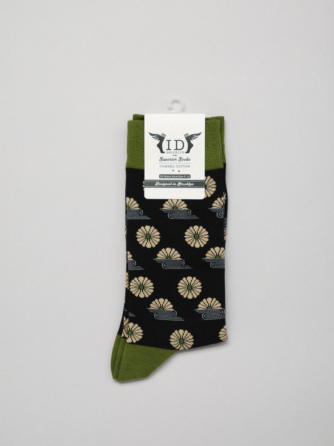 The Kiku Graphic Socks by ID Menswear feature a black base with beige floral patterns and green accents on the cuff, heel, and toe. Made from premium combed cotton for comfort, they come neatly folded with branding on the tag.