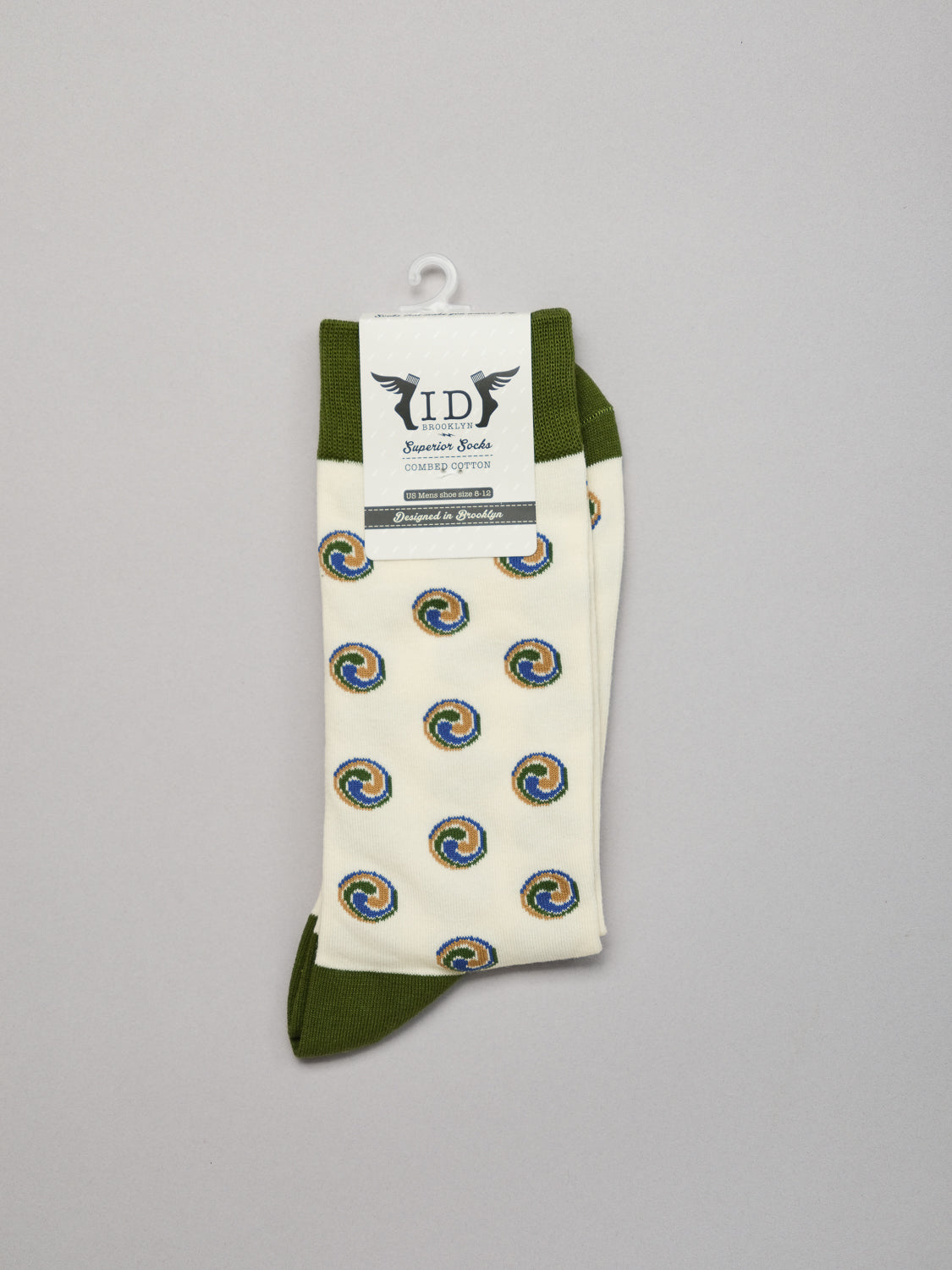 The Trinity Graphic Socks by ID Menswear feature a colorful Jacquard pattern in blue, yellow, red, and green with green cuffs and toes. Made from combed cotton, these stylish socks are showcased on a hanger against a plain gray background.