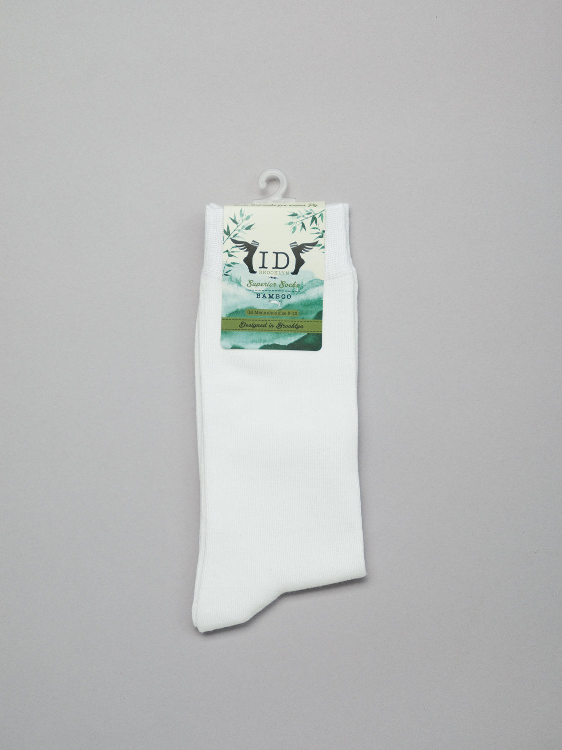 The Cylinder Knit Bamboo Solid Sock by ID Menswear features a breathable, eco-friendly green scenic design with bamboo illustrations. Highlighted against a plain grey background, the single white sock is neatly folded and displayed in IDS packaging with a plastic hanger at the top.