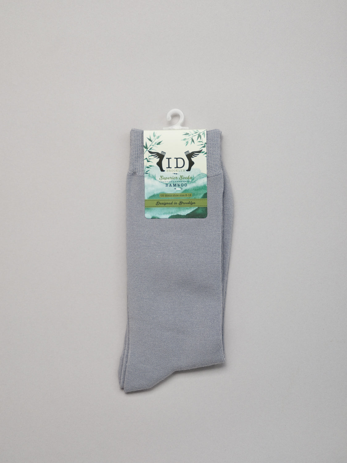A gray pair of Cylinder Knit Bamboo Solid Socks from ID Menswear hangs against a white background, featuring a scenic design label. These breathable, sustainable socks offer comfort and style while being eco-friendly.
