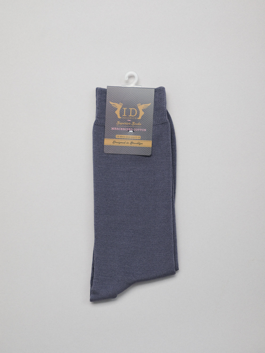 A single folded gray Mercerized Cotton Socks by ID Menswear, crafted from breathable fabric, hangs on a white hook. The attached label features elegant gold and silver text. Displayed against a plain white background, this luxury sock exemplifies elegance.