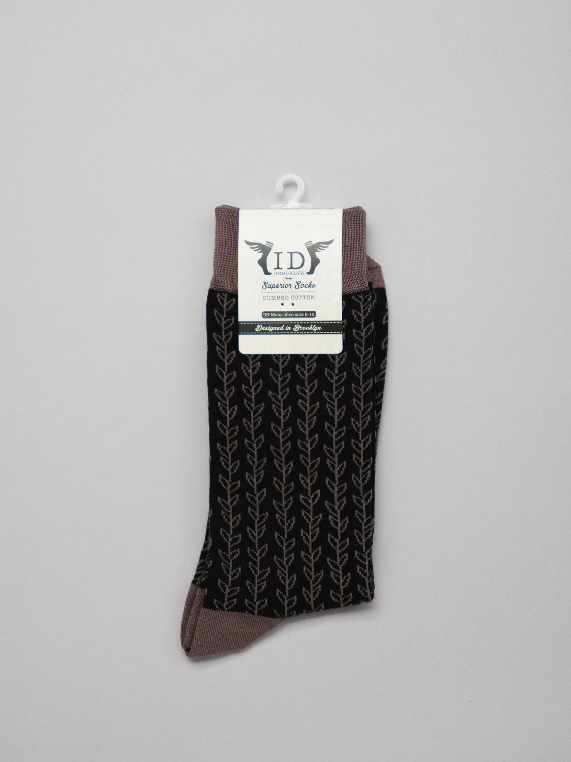 Explore the stylish Kombu Graphic Socks by ID Menswear. These breathable womens socks are crafted with combed cotton, featuring a black base with a leaf pattern, and muted brown trim at the toes, heel, and top. The packaging includes decorative wings and text.