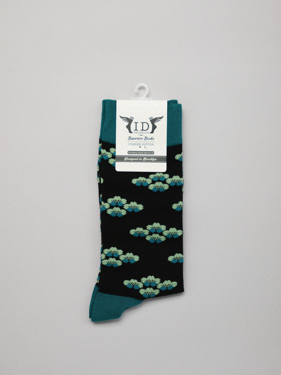 The Yuki Graphic Socks by ID Menswear are stylish black socks made from combed cotton, featuring turquoise and light blue floral patterns with teal cuff, heel, and toe. They come folded with an ID label on top against a light gray background.