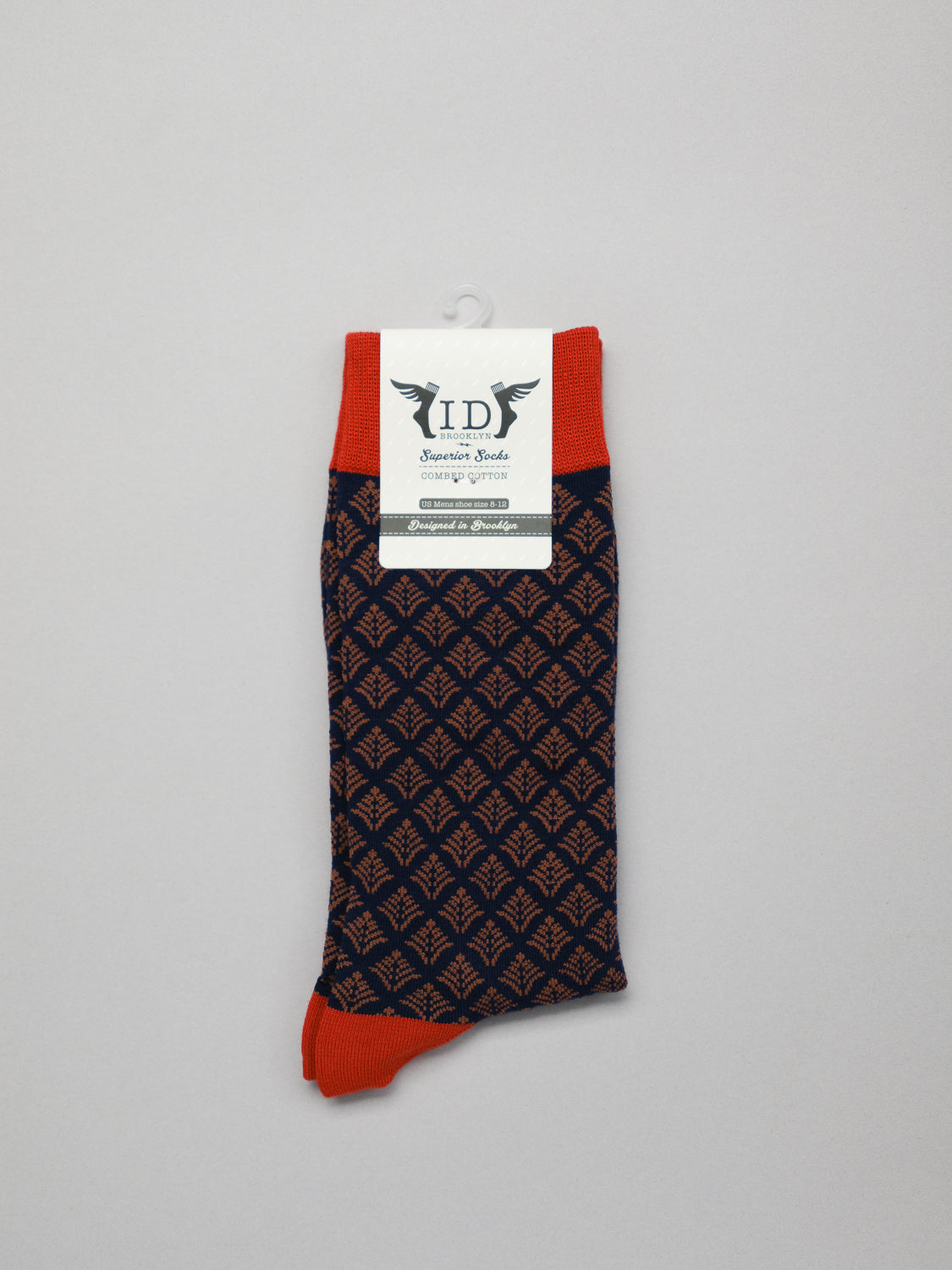 A pair of Retro Graphic Socks from ID Menswear, featuring a vintage-inspired black and orange pattern with solid orange heel and cuff, made from premium combed cotton. A label displays the initials ID and Retro Socks against a white backdrop.