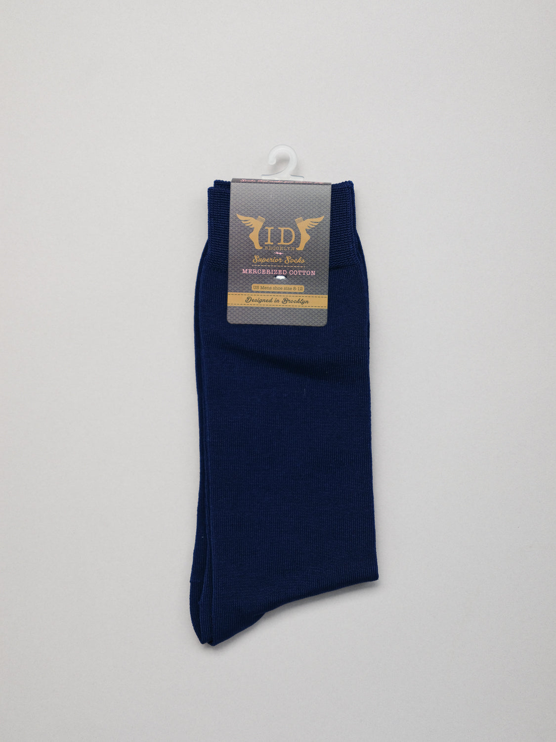 A pair of neatly folded dark blue Mercerized Cotton Socks by ID Menswear, featuring a beige label with lettering at the top. The label is attached to a white plastic hanger, set against a light gray background.