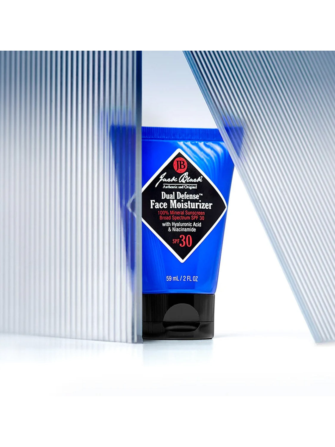 A blue tube of Jack Black Dual Defense™ Face Moisturizer 2 Oz stands behind two translucent ribbed acrylic panels, with only the center of the oil-free, mineral SPF moisturizer clearly visible.