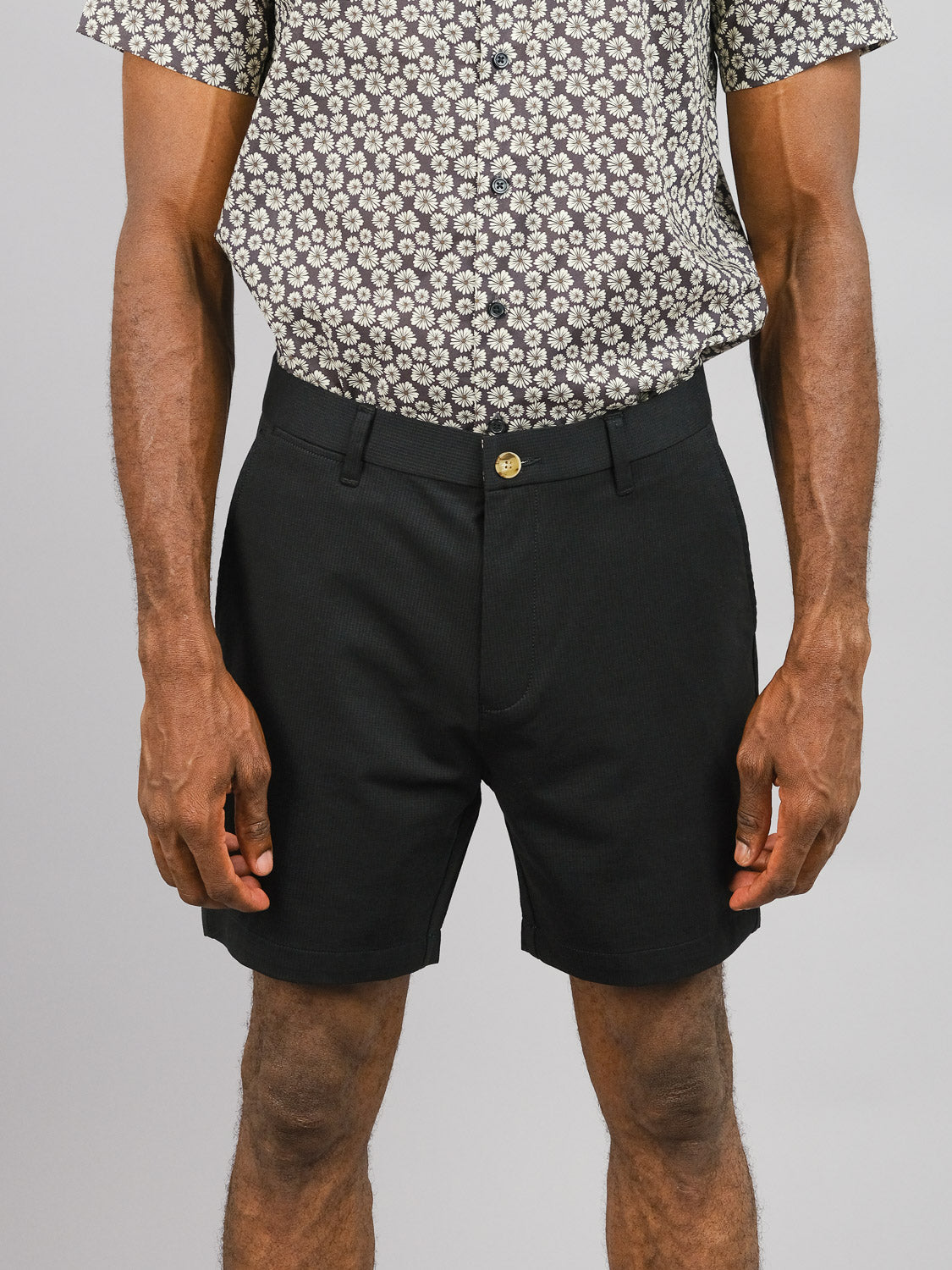 A person in a short-sleeved patterned button-up and ID Menswear’s Eckford 5 Inseam Stretch Short stands against a plain light gray background, shown from shoulders to mid-thigh.