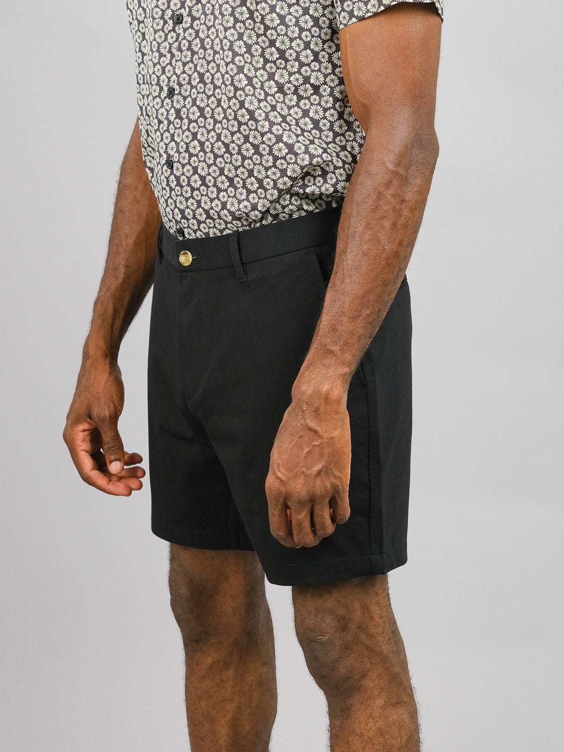 A man wears a patterned short-sleeve shirt and ID Menswear’s Eckford 5 Inseam Stretch Short, standing against a plain light gray background with his arms relaxed at his sides for comfortable, casual style.