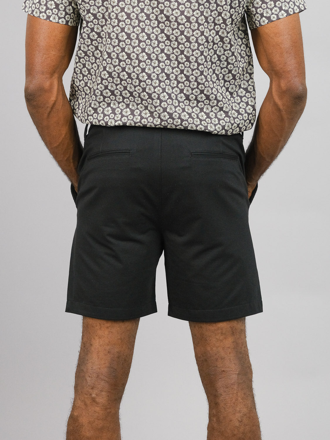 A person stands facing away, wearing a patterned short-sleeve shirt and ID Menswear’s Eckford 5 Inseam Stretch Short. Cropped from shoulders to knees, the image highlights the laid-back style and comfort of this casual look.
