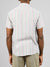 The person showcases the back of the outfit featuring ID Menswears Streak Cotton Shirt—a short-sleeved, lightweight, multicolored striped cotton shirt in a regular fit—paired with beige pants against a light gray backdrop.