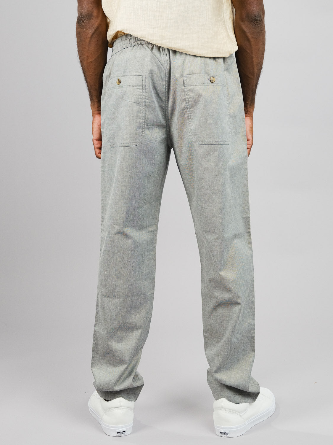 A person, facing away from the camera, models ID Menswears Kruger Relaxed Pant in light grey with back pockets and drawstring. Paired with white sneakers and a light-colored shirt, this lightweight ensemble is perfect for warm weather.