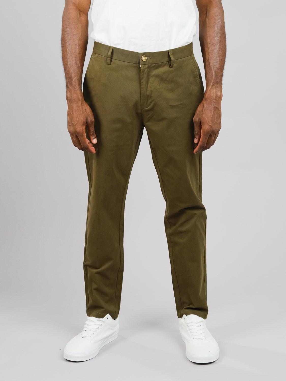 A person stands against a plain backdrop wearing a white shirt with olive green ID Brooklyn Chino pants by ID Menswear, crafted from cotton twill. Paired with white sneakers, only the torso and legs are visible, highlighting the regular slim fit.