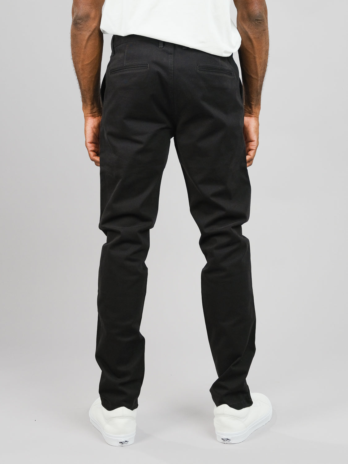 Sporting ID Menswears ID Brooklyn Chino, a person is seen in regular slim fit black pants and white sneakers, posing against a plain gray background and capturing a casual yet stylish look.