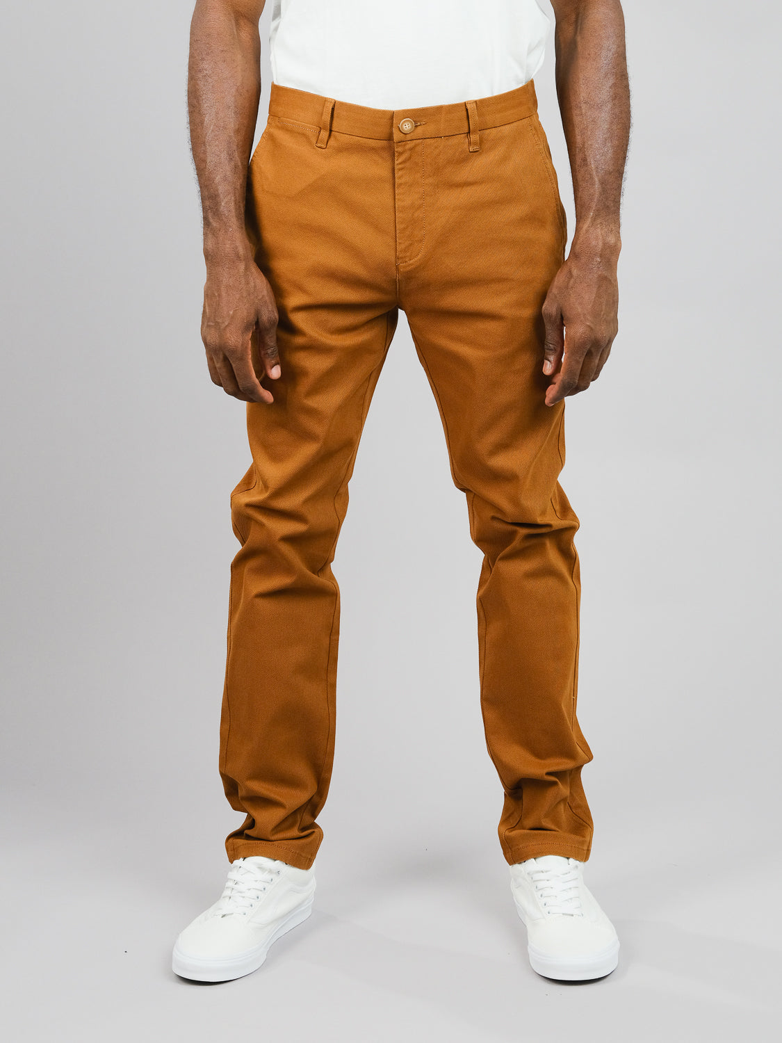 A person wearing ID Menswears Wythe Twill Stretch Chino and white sneakers stands against a plain gray background, showcasing the lower half of the body and stylish comfort, ready for casual occasions.