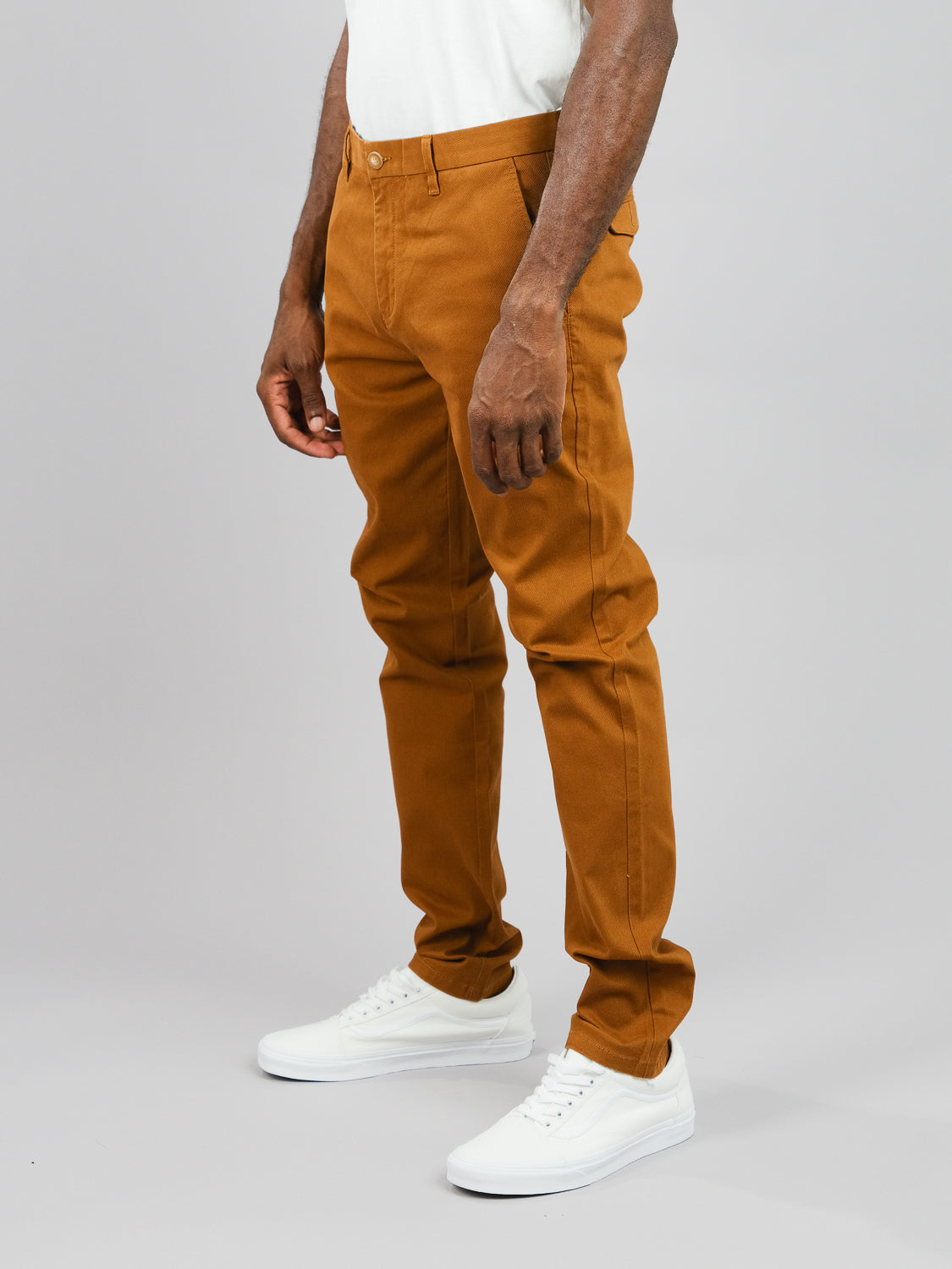 A person stands against a gray background wearing ID Menswears Wythe Twill Stretch Chino; their white shirt, slim-fit pants, and white sneakers capture the cotton twill texture and color contrast, perfect for casual occasions while highlighting the clothings style.