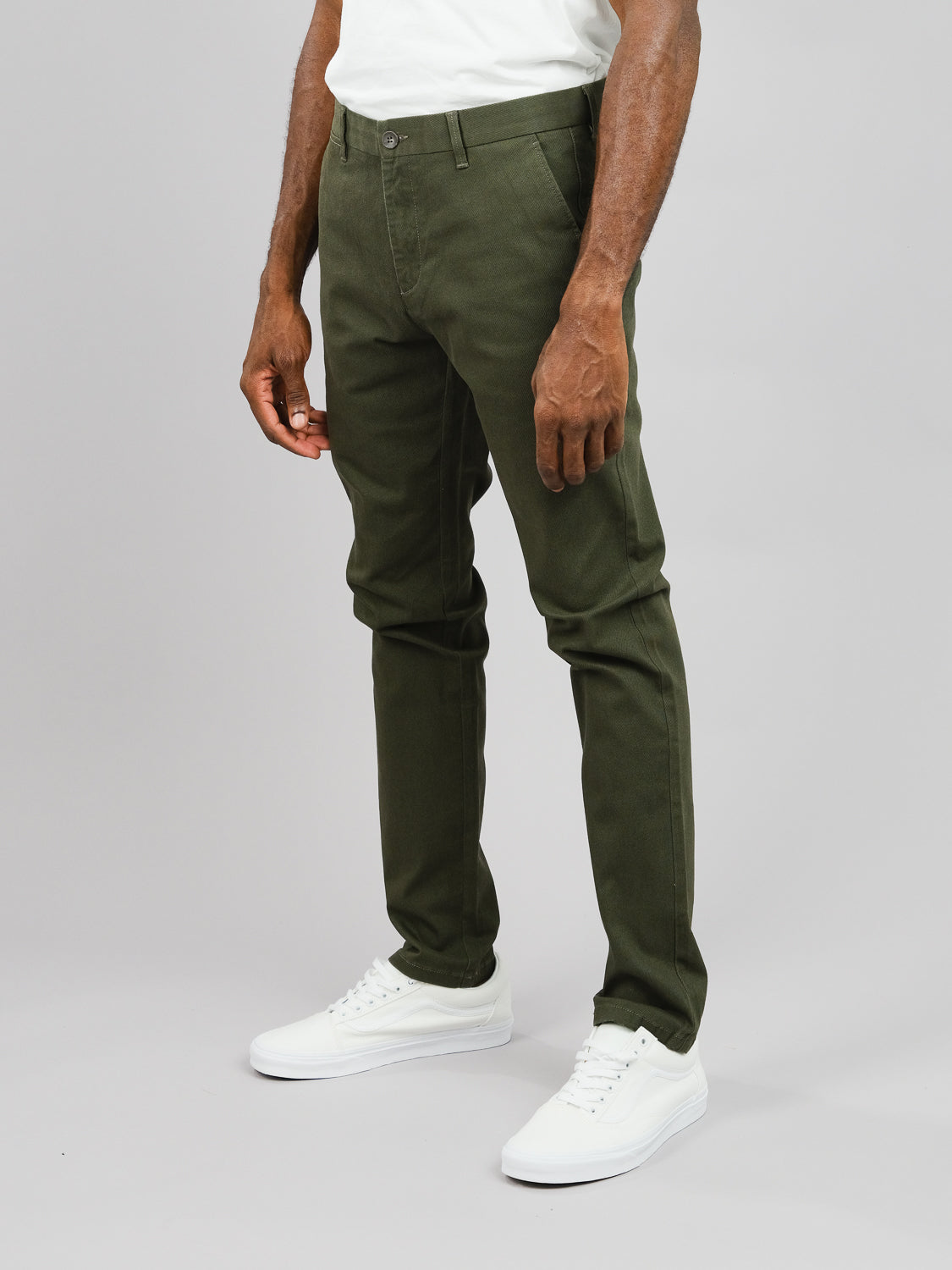 Against a plain background, someone showcases the olive green Wythe Twill Stretch Chino pants by ID Menswear. These slim-fit cotton twill chinos are paired with a crisp white shirt and sneakers, perfectly illustrating their casual style and fit.