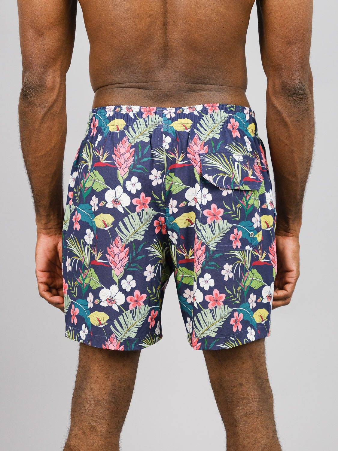 A person, back to the camera against a plain background, wears colorful floral-patterned Kipukai Fast Dry 4-Way Stretch Swim Trunks by ID Menswear, made from recycled plastic bottles with quick-dry technology.