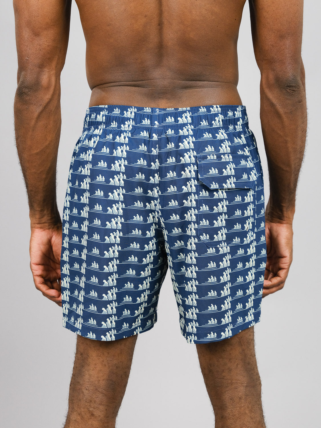 A person models the Tsunami Fast Dry 4-Way Stretch Swim Trunk by ID Menswear, featuring a blue and white sailboat design made from recycled plastic bottles, against a plain gray background.