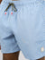 A close-up of a person wearing ID Menswear’s Stars Fast Dry 4-Way Stretch Swim Trunk, featuring a light blue geometric pattern, green drawstring, rectangular logo patch near the hem, and quick-dry fabric made from recycled plastic bottles.