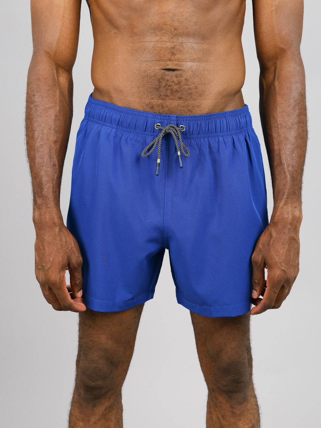 A person in ID Menswears Oyogu Quick Dry 4 Way Stretch Swim Trunk with a black and white drawstring is against a gray backdrop, visible from neck to knees.