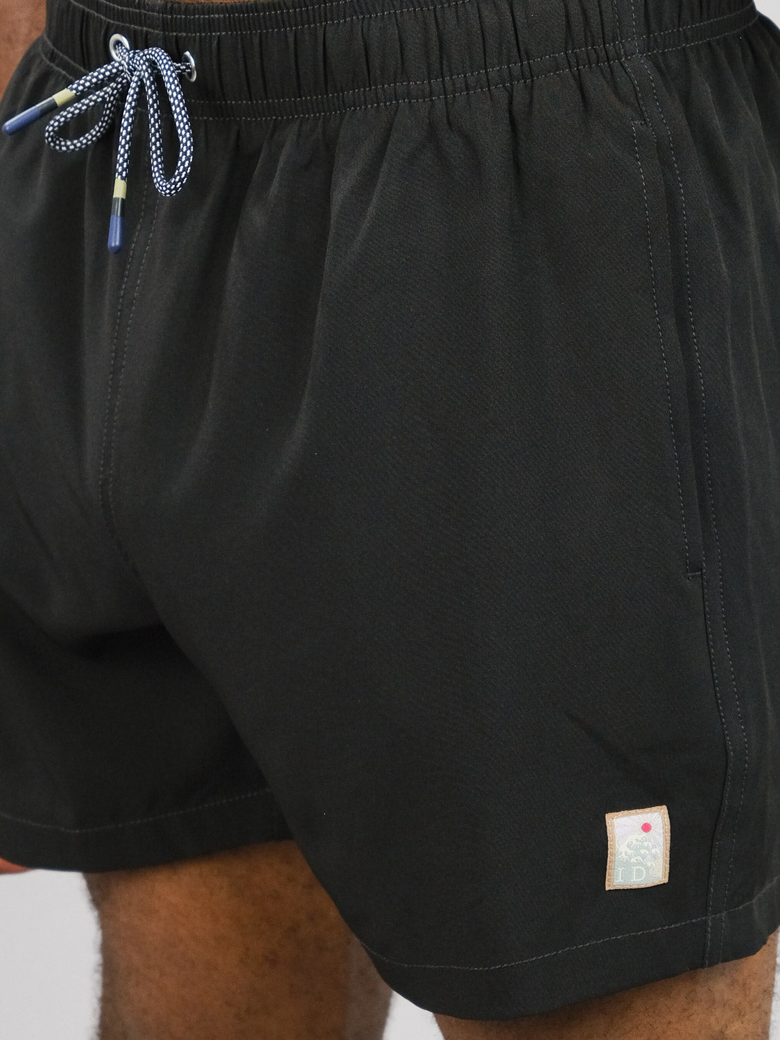 Close-up of a person wearing ID Menswear’s Oyogu Quick Dry 4 Way Stretch Swim Trunk, featuring a small label near the hem and a blue-and-white drawstring at the waistband.
