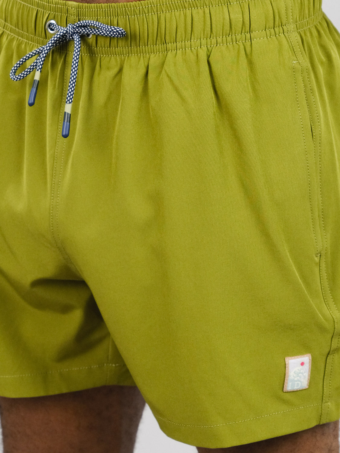 Close-up of a person wearing ID Menswears Oyogu Quick Dry 4 Way Stretch Swim Trunk in olive green, featuring a white and black drawstring and a small patch near the left leg’s hem.
