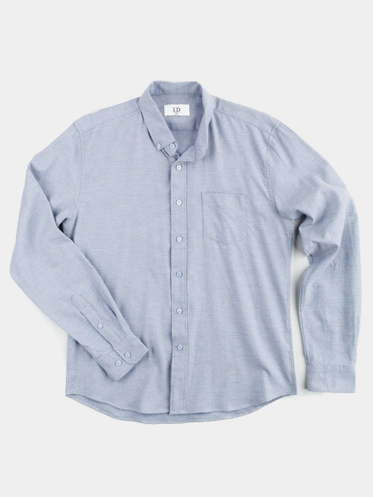 The Amir Solid Flannel Textured Dobby Shirt by ID Menswear is a light blue, long-sleeve button-up with a collar and chest pocket. Crafted in a dobby weave for comfort, it includes buttons on the sleeve cuffs and lays flat against a white background, showcasing its neat, classic style.