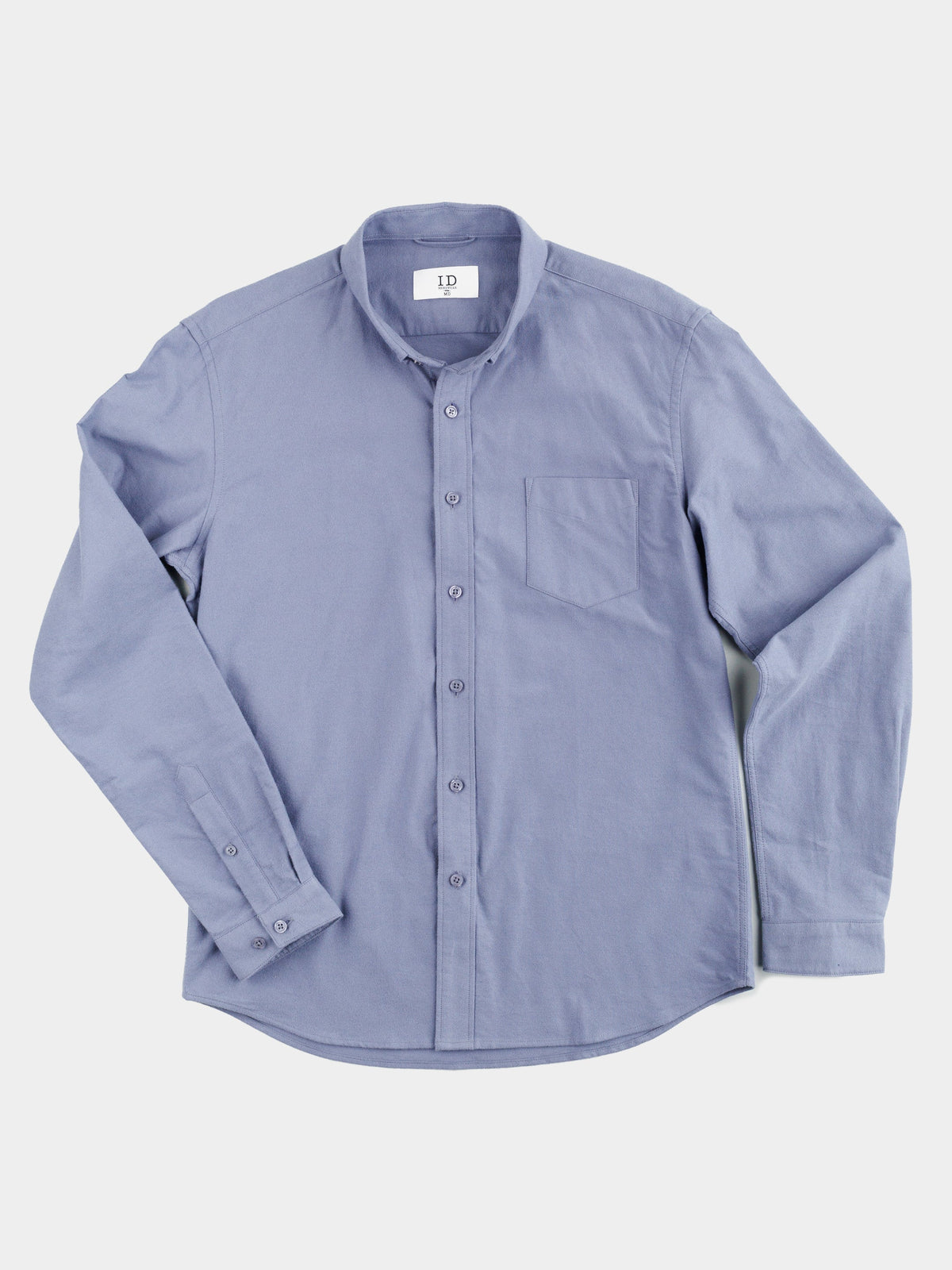 The Milo Brushed Oxford Flannel Cotton Shirt by ID Menswear, in light blue, features a single chest pocket and long sleeves. Its casual style is highlighted by small buttons down the front and is laid flat on a white background.