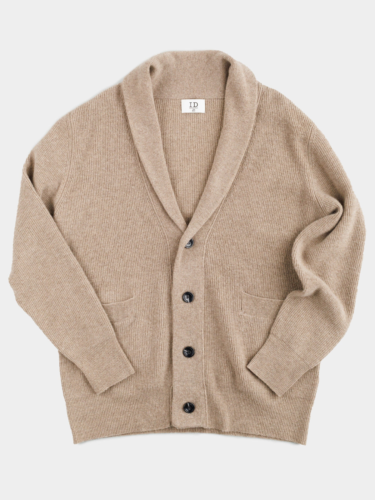 The Basecamp Cashmere Merino Cardigan by ID Menswear is a luxurious beige, ribbed-knit piece with long sleeves, a shawl collar, and five dark buttons. It features two front pockets and is crafted for your winter wardrobe. The cardigan lies flat on a light gray background.