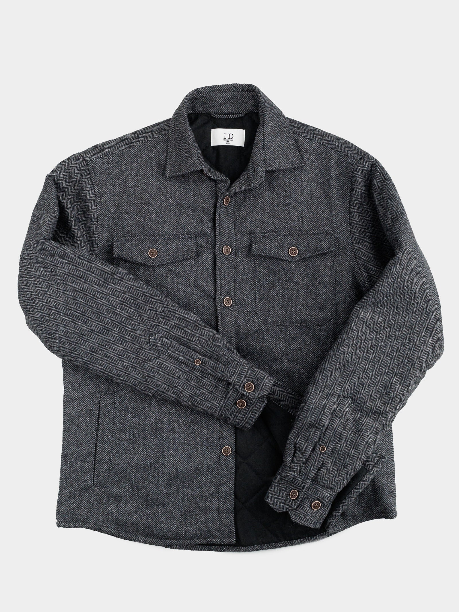 The Stuntman Wool Blend Tweed Jacket by ID Menswear is a dark gray, long-sleeve jacket featuring two chest pockets, brown buttons, and a quilted lining, shown laid flat on a light background.