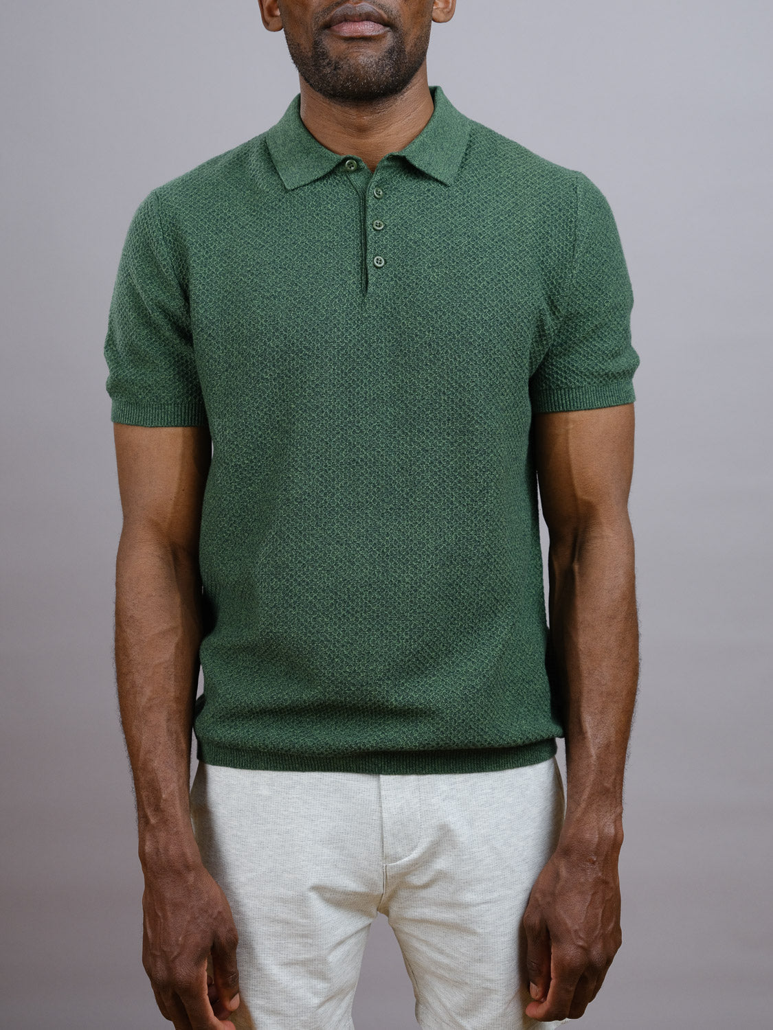 A man stands against a plain gray background, wearing the Tucson Knitted Cotton Polo by ID Menswear and light-colored pants. His face is partly out of frame, emphasizing the shirt’s comfortable, breathable fit.