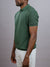 A man in the ID Menswear Tucson Knitted Cotton Polo, featuring a textured green knit, pairs it with light beige shorts against a plain gray background—showcasing refined casual style.