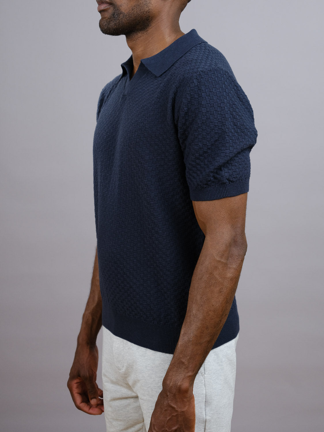 A man in the Cairo Knitted Cotton Polo by ID Menswear and light-colored pants stands slightly turned against a neutral gray background, perfectly showcasing the polo’s effortless, premium casual style.