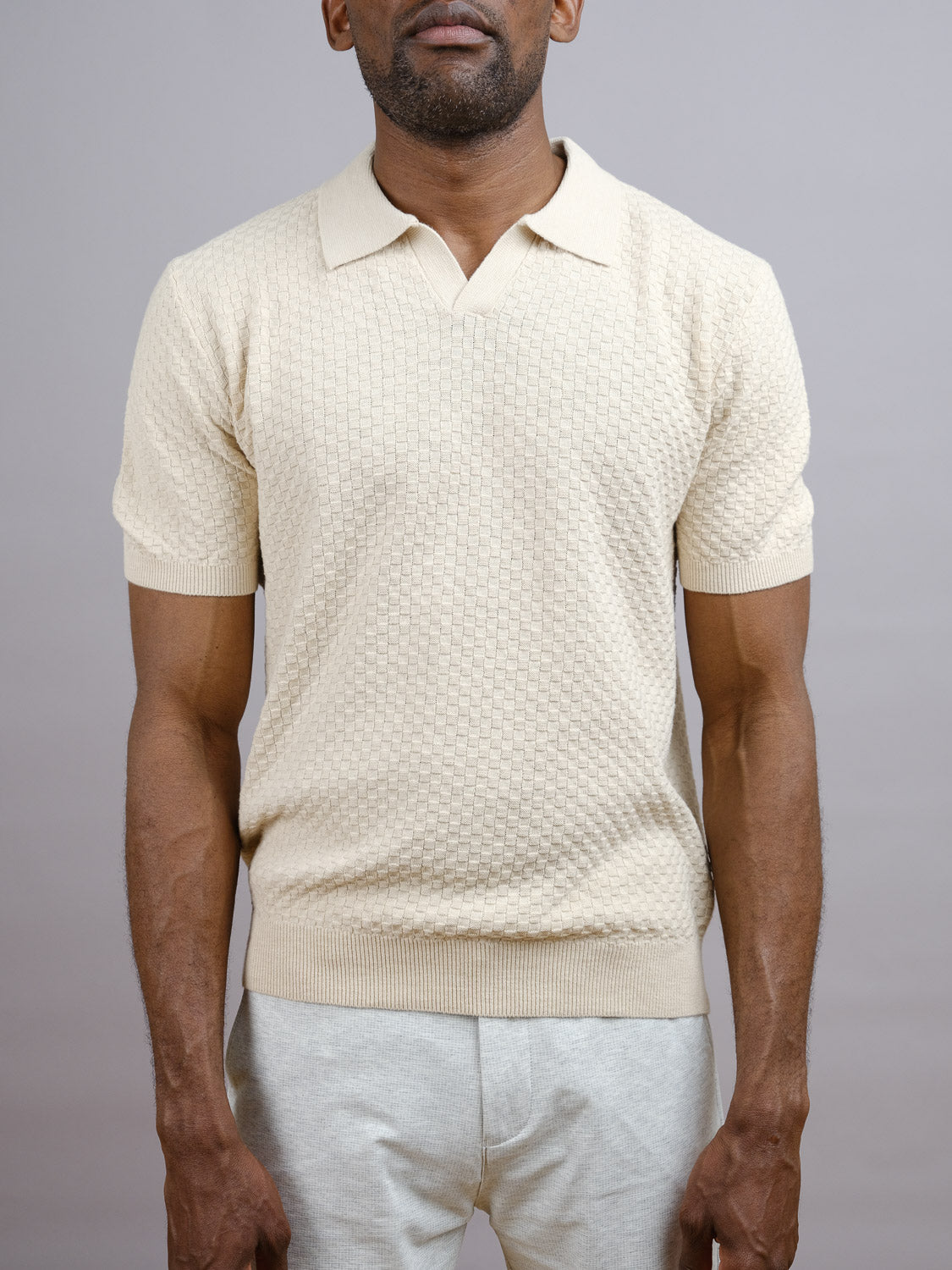 A man models the Cairo Knitted Cotton Polo by ID Menswear with light-colored pants, standing against a plain light gray background. His partially visible face emphasizes the refined casual style of this premium cotton polo.