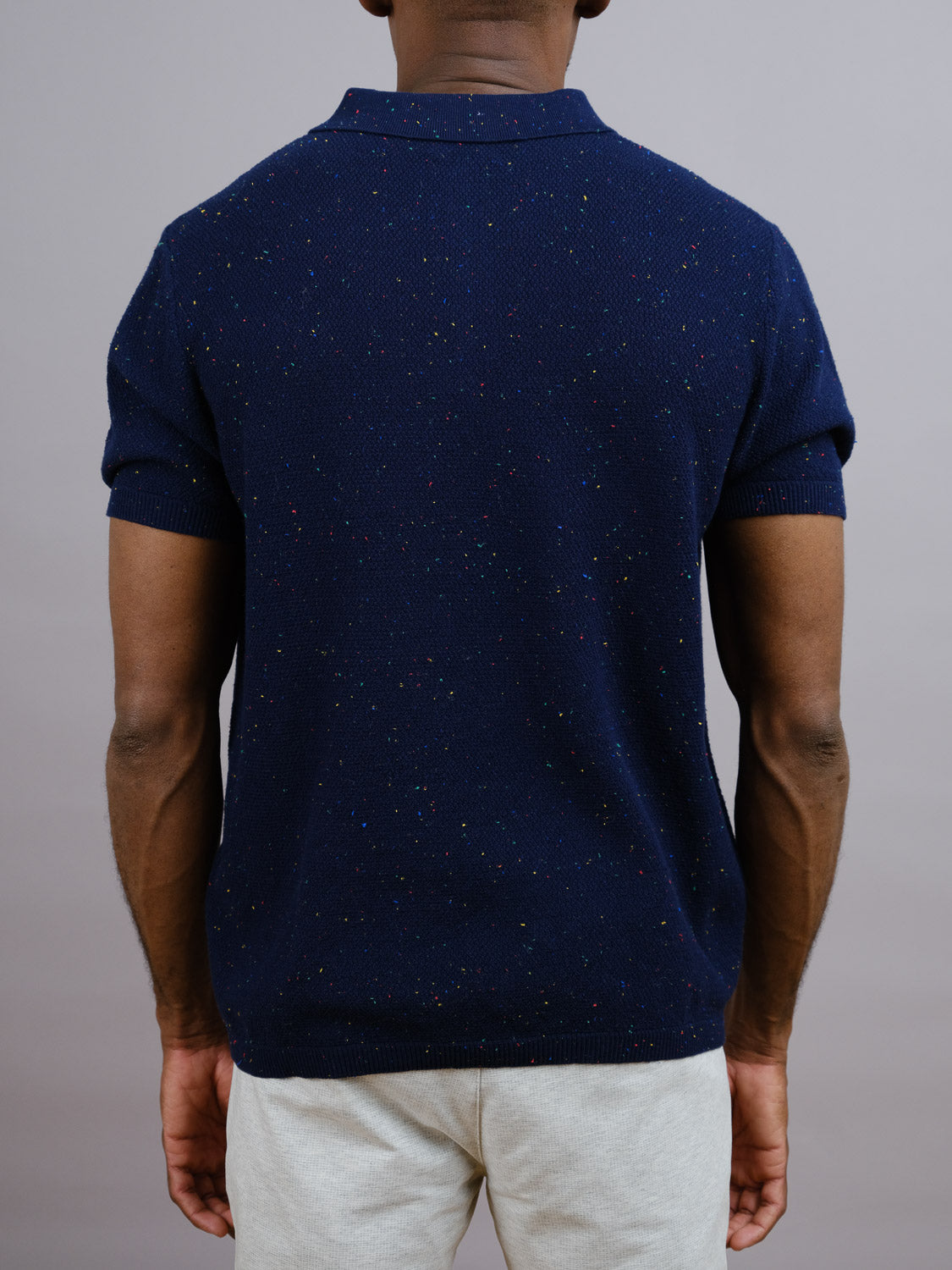 With their back to the camera, a person wears ID Menswear’s New Austin Knitted Cotton Polo in dark navy with light pants against a plain gray background—a great pick for casual style.