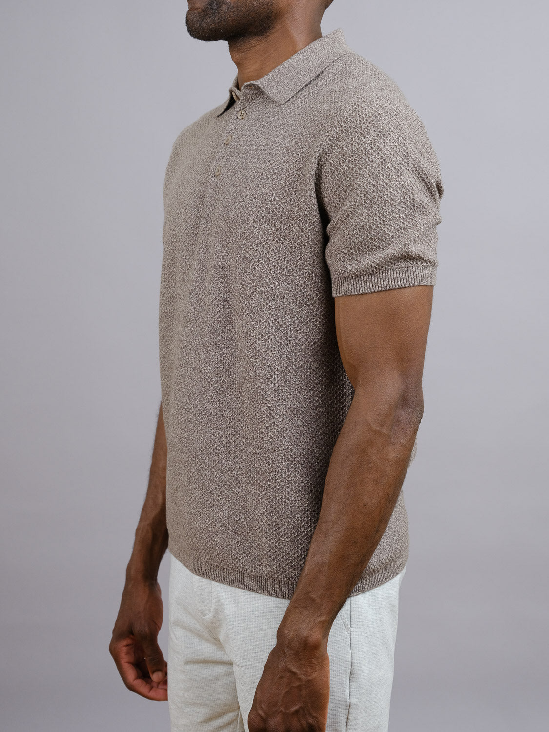 A man in the Tucson Knitted Cotton Polo by ID Menswear and light-colored pants stands in side profile against a gray background—a stylish, breathable choice for casual wear.