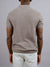 A man faces away, wearing the Tucson Knitted Cotton Polo by ID Menswear in textured light brown with light pants—exemplifying casual, breathable style against a plain gray background.