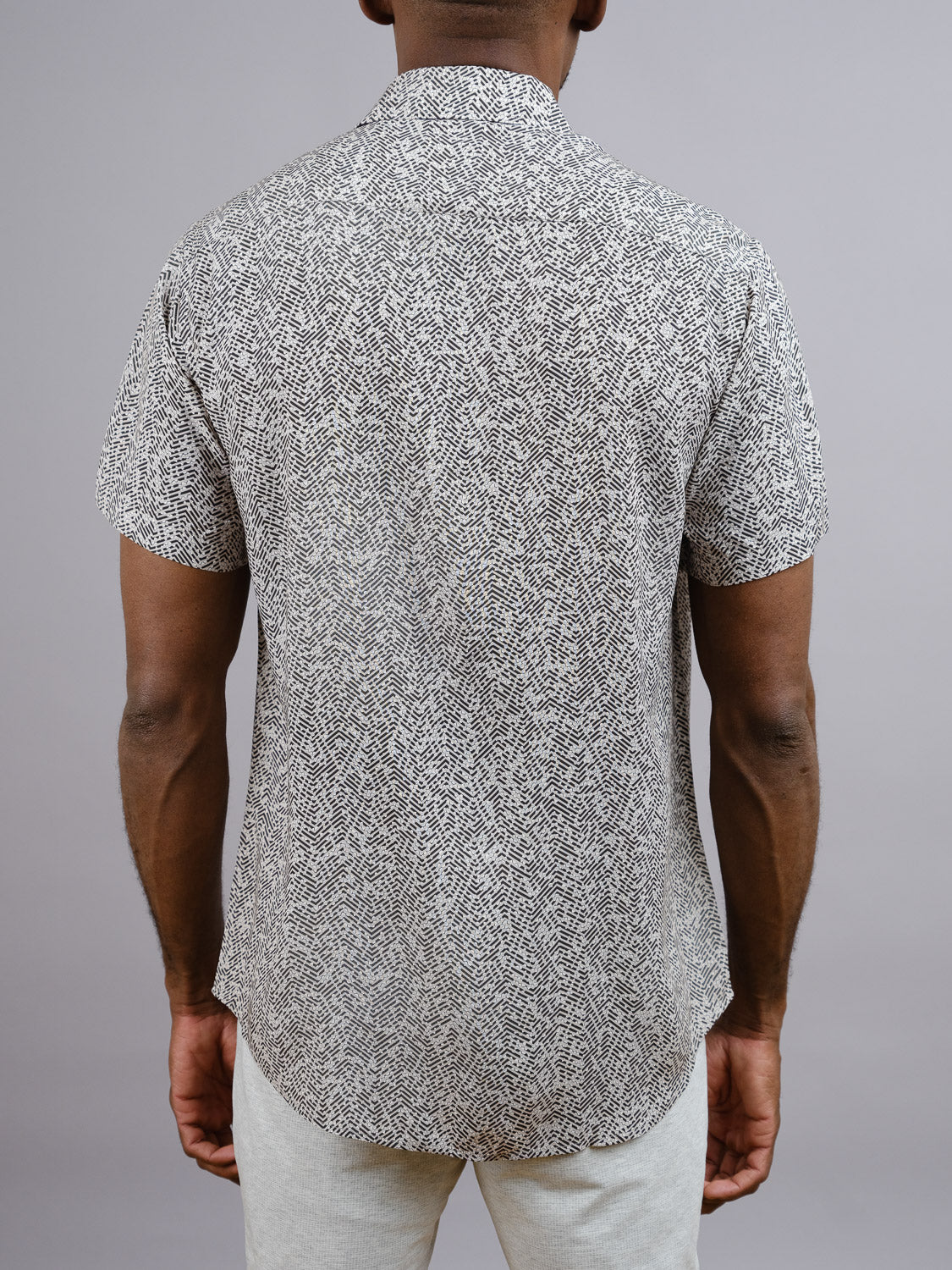 A person stands with their back to the camera, wearing the Kikaga Geometric Print Shirt by ID Menswear and light pants—an easy, stylish outfit for warm days against a plain gray background.