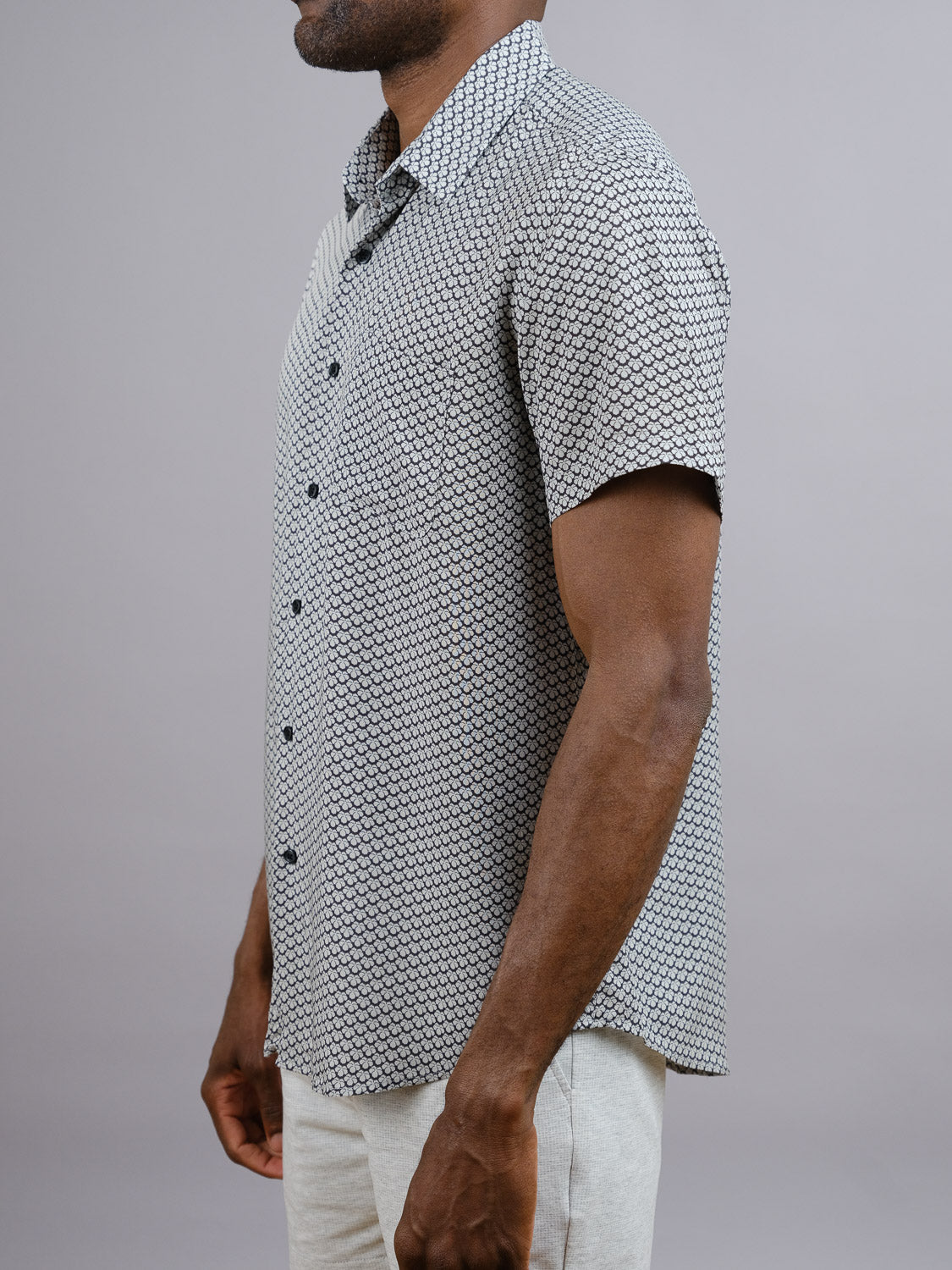 A man wears the Toyo Japanese Print Shirt by ID Menswear—a lightweight, short-sleeve rayon top with vibrant patterns—and light pants, standing sideways against a plain gray background with his head partially out of frame.